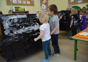 Dzieci malują na czarnej folii białą farbą zimowy krajobraz